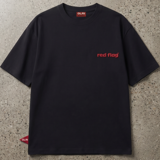 A black short-sleeve crewneck t-shirt with 'red flag' printed in red on the left chest, laid flat on a textured gray concrete surface. The brand 'OLRI' is visible on the inner neck label and a small red tag near the bottom left hem.