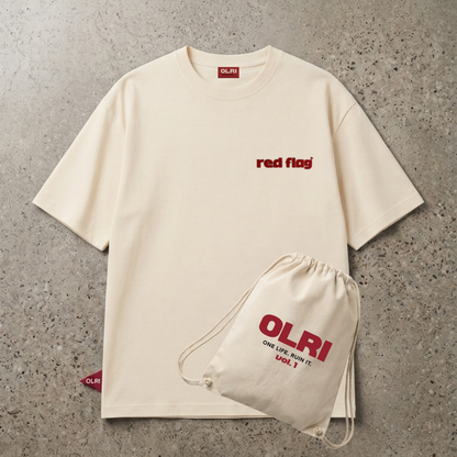 An off-white short-sleeve t-shirt with 'red flag' printed in red on the left chest, shown flat-laid on a textured gray concrete background alongside a matching off-white drawstring bag with red OLRI branding.