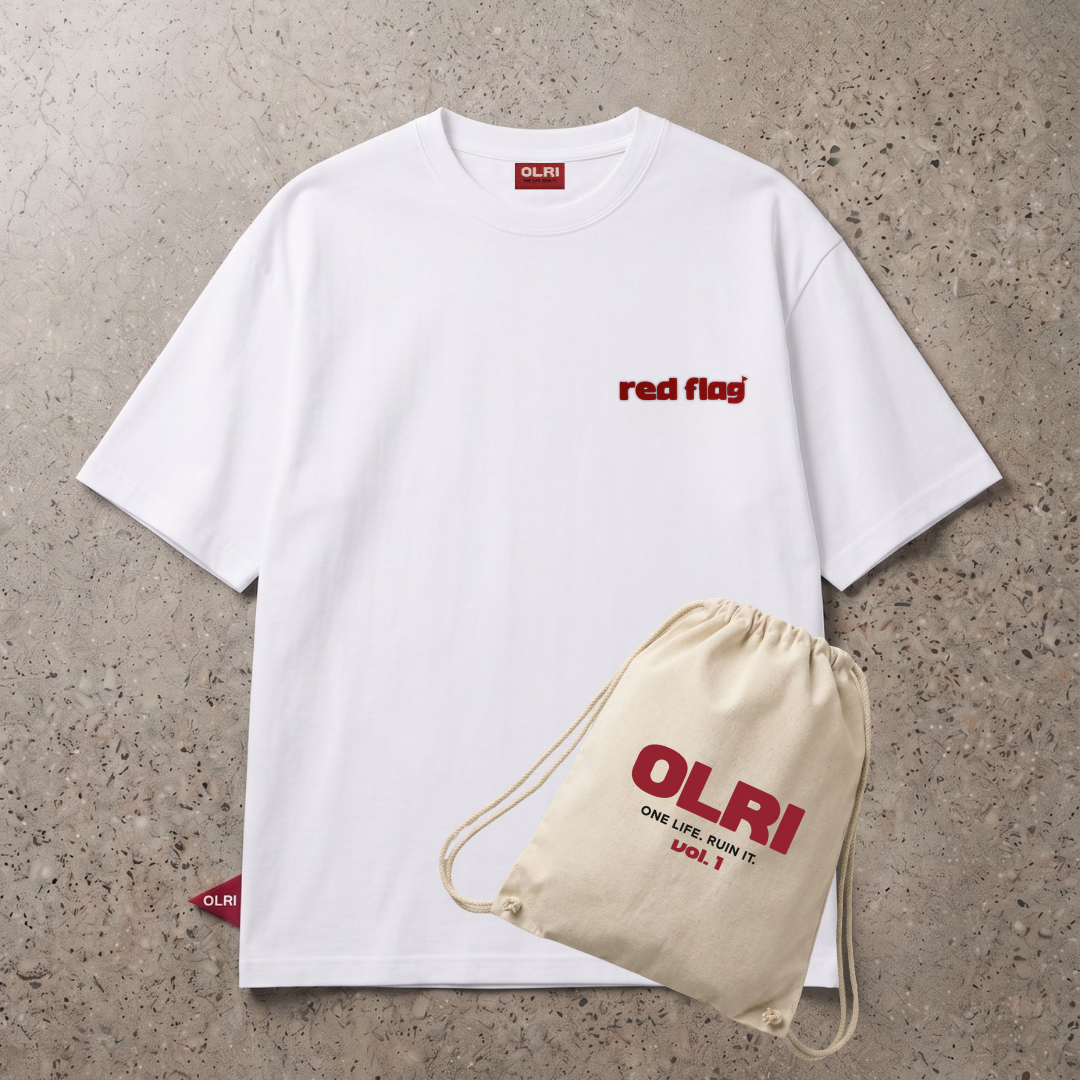 A white short-sleeve T-shirt with a small red 'red flag' logo on the chest, laid flat on a textured gray surface. A beige drawstring pouch with red 'OLRI' branding is placed in front of the shirt.
